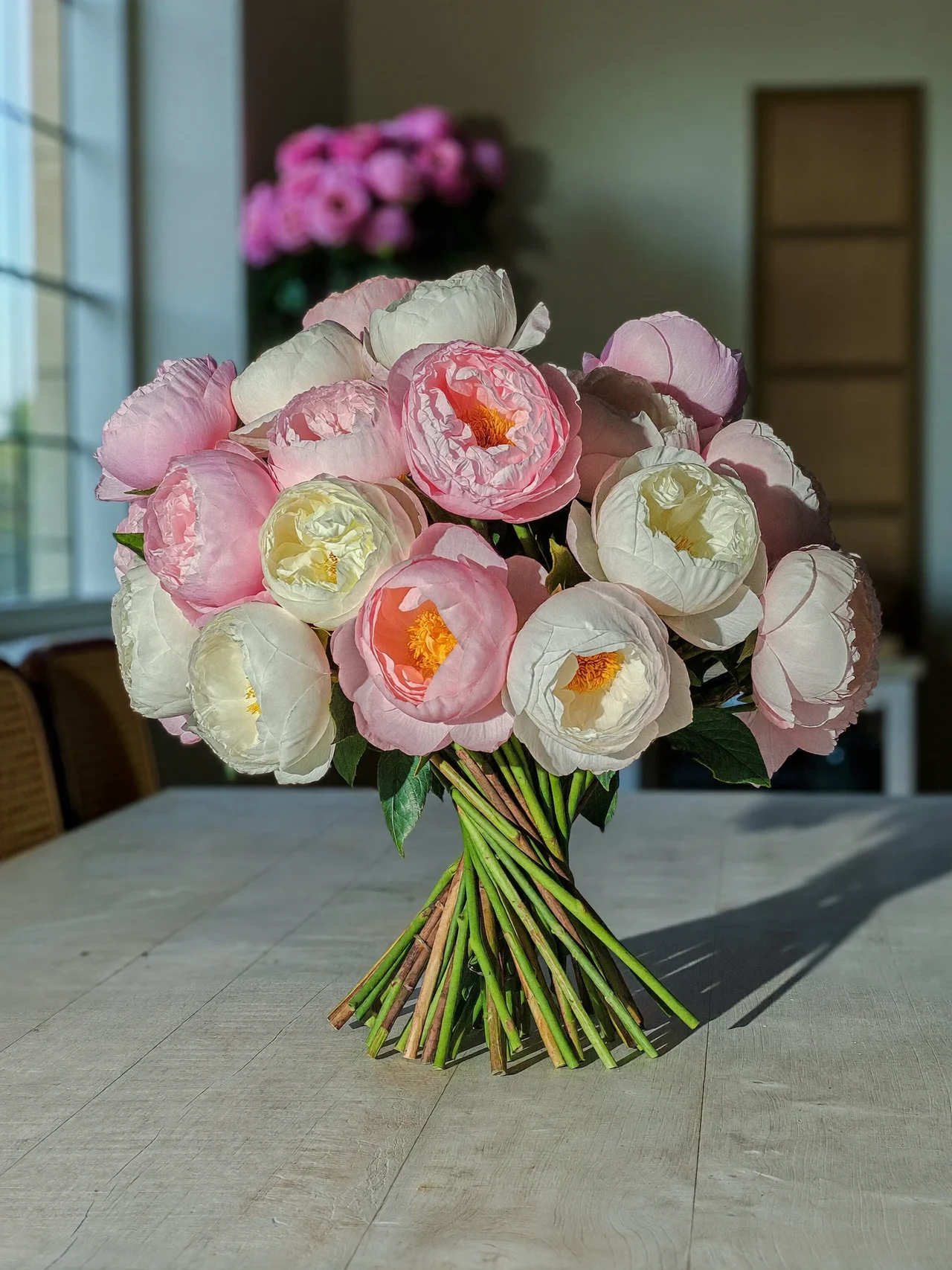 Illustration eines pastellfarbenen Pfingstrosen- und Rosenstrausses auf einem hellen Holztisch