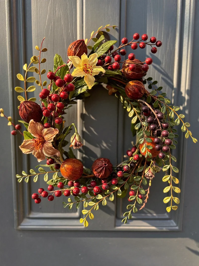 Illustration eines saisonalen Kranzes aus Beeren und Blüten an einer Holztür