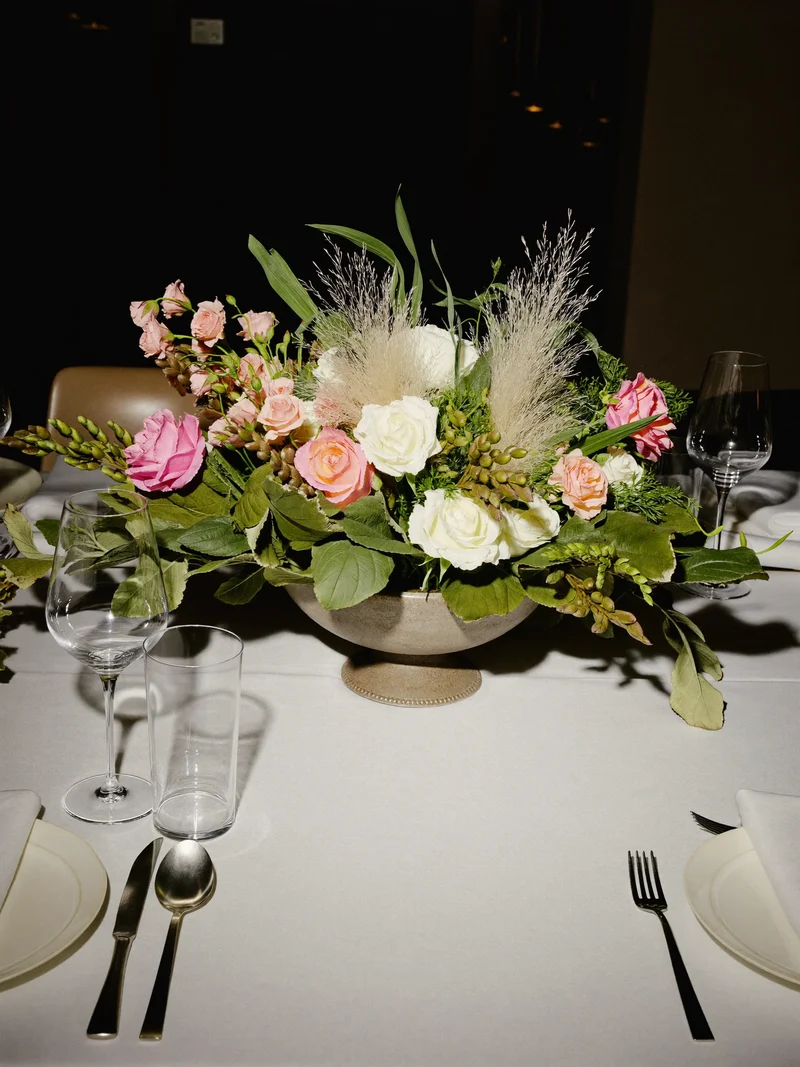 Illustration eines Kunstblumen-Arrangements in steingrauer Schale auf gedecktem Esstisch